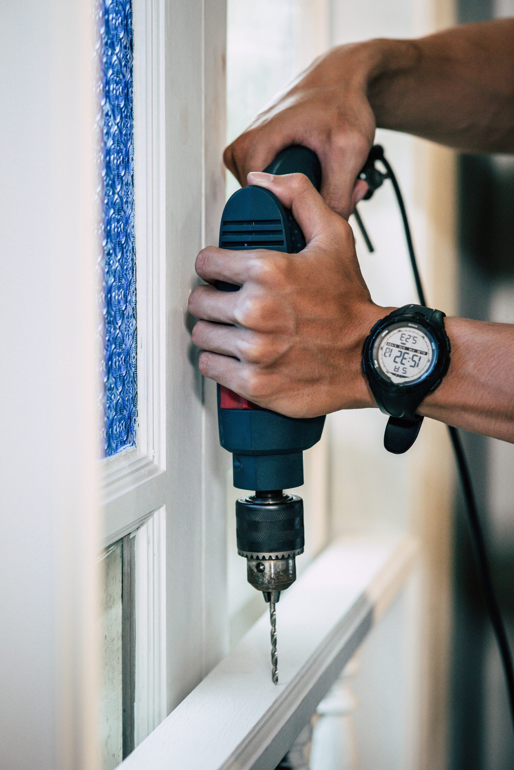 The carpenter holds the drill and drills the window.